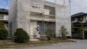 足場と養生シートのかかった日本の住宅で外壁塗装をする職人